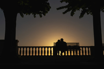 Silhouette of a kissing couple in love on a sunset background. Palm trees and a bench. Sea view point. Vacation and tourism concept, travel. The relationship. Happy together. Italy.