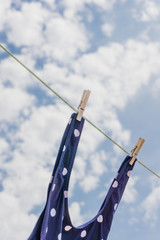 Close up view of a  cute swimsuit strap hanging in a clothes line with a clothespine against blue sky.
