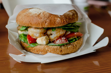 hamburger with dark flour with vegetables and shrimp on a wooden background