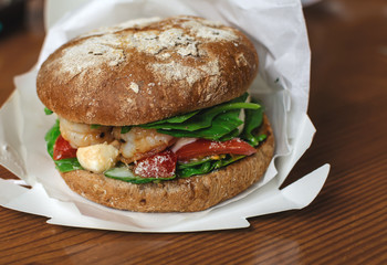 hamburger with dark flour with vegetables and shrimp on a wooden background
