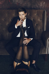 Elegant man in a black suit. Couple at home. Hot woman in a black underwear. Male with cigar