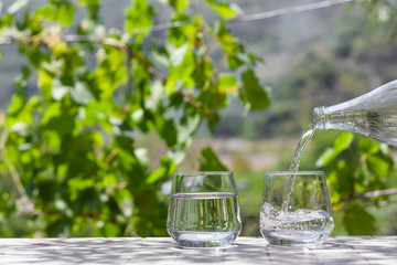 Fersh, clean, drink water pouring in to glass from a glass bottle. Select focus blurred nature background. Healthy lifestyle, water balance control, skin care concept