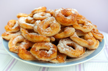a pile of sweet Golden-brown doughnuts (doughnuts) with white powdered sugar lies in a white plate on a light background close-up