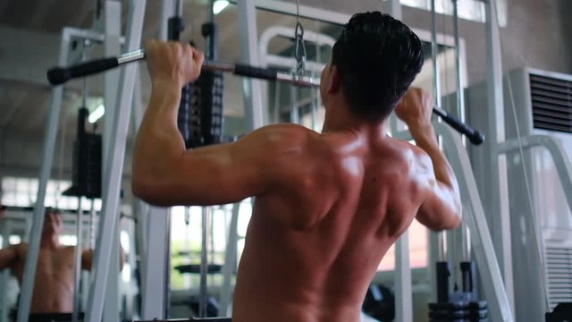 Attractive back of muscular sport man exercise by machine of pulling the weight and he try hard with heavy weight in gym. Concept of workout to get good health and strong body to prevent disease.