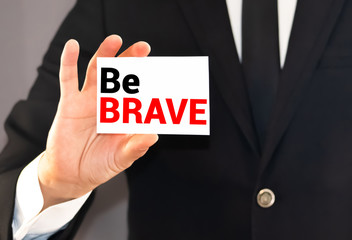 Obraz premium A person writes text, a word, the phrase Be Brave with marker on a light background. Business concept.