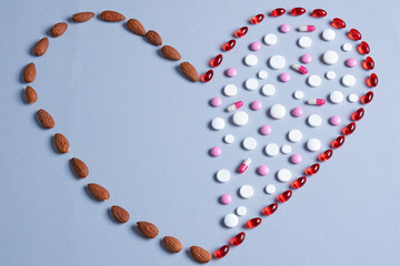 Healthy eating concept. Crooked heart made from pills and almonds. Healthy fats and red and white pills on gray background