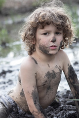 A little boy is playing in the mud. He is covered in dirt and mud, screaming and yelling. Boyhood outside, getting dirty. No rules for this child. Wild child, freedom 