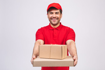 Image of a happy young delivery man in red cap standing with parcel post box isolated over white background.