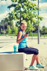 Portrait of young attractive woman sitting while using and listening to music on her smartphone in park
