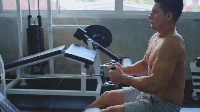 Side view of muscular sport man working out on rowing machine in gym and he look happy and concentrate with the activity. Concept of good health for better lifestyle and prevent covid virus infection.