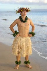 Male hula dancer poses with hand on hops at sunset by the beach. - obrazy, fototapety, plakaty