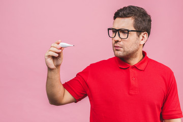 Virus concept. Young caucasian man holding a thermometer isolated over pink background.