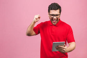 Happy winner. Image of happy young bearded man standing over pink background isolated. Using tablet computer.