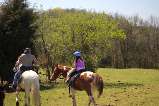 Young woman riding a paint horse with instructor navigating in the right direction