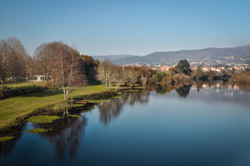 The river through the park and the city is reflected in the water. In the background of mountain and city. Ponte de Lima Portugal.