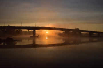 Wschód słońca i most nad rzeką spowite w oparach magicznej mgły. 