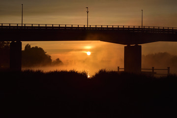 Wsch&oacute;d słońca i most nad rzeką spowite w oparach magicznej mgły. 