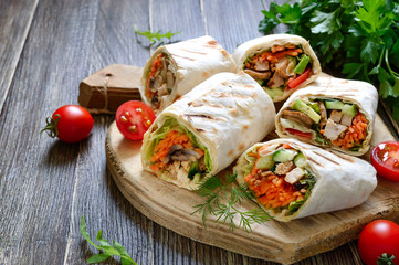 Fresh tortilla wraps with chicken, mushrooms and fresh vegetables on wooden board. Chicken Mexican burrito. Tasty appetizer. Dishes from pita bread. Healthy food concept