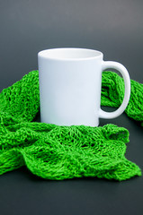 White coffee mug nestled in green lace scarf on a dark background with copy space for text or graphics.  Handknit lace scarf fashion accessory.