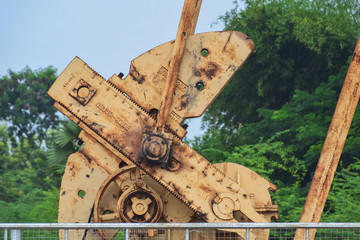 Old rusty oil pump jack machinery with rough surface and texture in natural green location