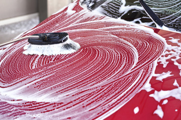 Red car front hood washed in self serve carwash, detail on brush leaving strokes in white soap foam