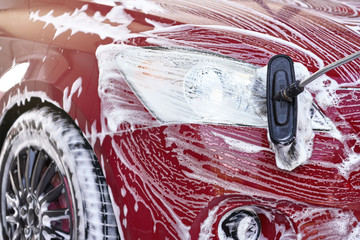 Detail on red car front light washed in self serve carwash, white soap strokes on surface