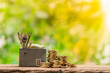 Home models and gold coins and tools, construction equipment and spanners for building or repairing houses put on the wooden table in garden, Loan for restoration real estate concept.
