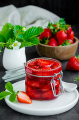 Homemade strawberry jam in a glass jar with fresh strawberries on a dark wooden background. Rustic style. Vertical orientation.