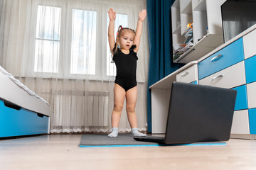 the child does gymnastics on a gymnastic rug at home in front of a computer. distance learning sports