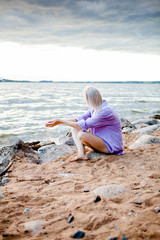 blonde girl sitting on the beach and pouring sand