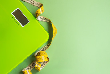 Green scales and yellow measuring tape on a green background. The concept of normal weight and health control. The horizontal position, lay flat, copy space