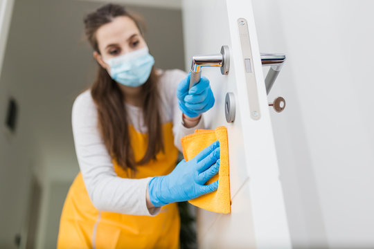 Close Up Of Woman With Protective Mask Cleaning Door. Coronavirus Prevention Concept.