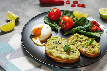 Healthy toast with avocado mexican sauce guacamole, boiled egg, cherry tomatoes and salad on concrete background.