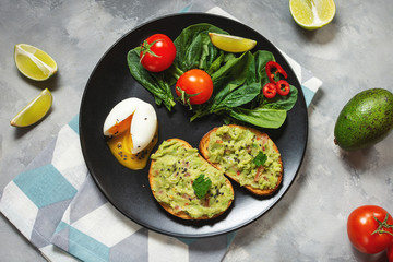 Healthy toast with avocado mexican sauce guacamole, boiled egg, cherry tomatoes and salad on concrete background. Top view