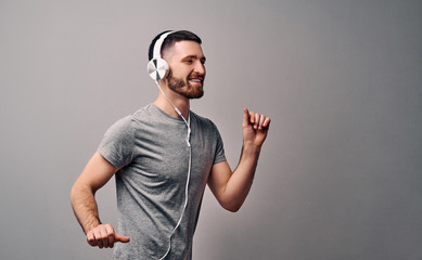 Dance to your favorite song in your favorite headphones.Beautiful young man dancing on a gray wall background.Copy space.