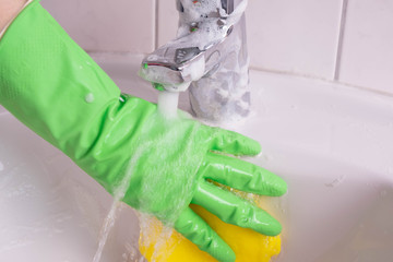woman in gloves cleans the sink and water tap in the bathroom
