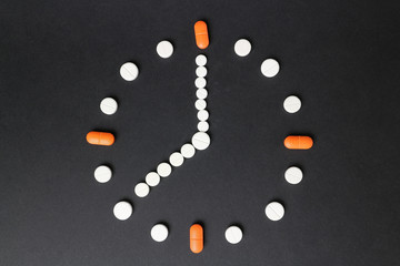 The watch is lined with tablets on a black background and shows eight hours. Medical concept. 