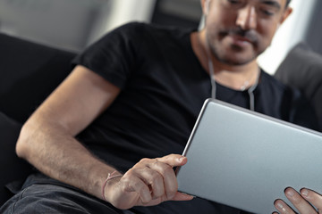 man holding using digital tablet and headphones sitting on a sofa. Online education, working, video call