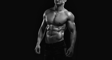 Fototapeta na wymiar Muscular model sports young man on dark background. Black and white fashion portrait of strong brutal guy. Sexy torso. Male flexing his muscles. Sport workout bodybuilding concept.