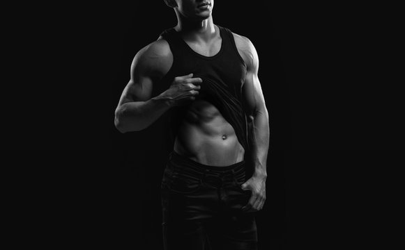 Muscular model sports young man on dark background. Black and white fashion portrait of strong brutal guy. Sexy torso. Male flexing his muscles. Sport workout bodybuilding concept.