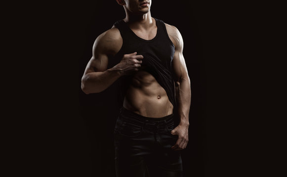 Muscular model sports young man on dark background. Fashion portrait of strong brutal guy. Sexy torso. Male flexing his muscles. Sport workout bodybuilding concept.