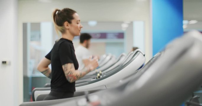 Young woman running on a treadmill at gym. Side view. Woman training at fitness center. Woman exercising cardio workout