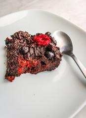 Chocolate brownie slice on a white plate with a spoon. Vegan brownie.