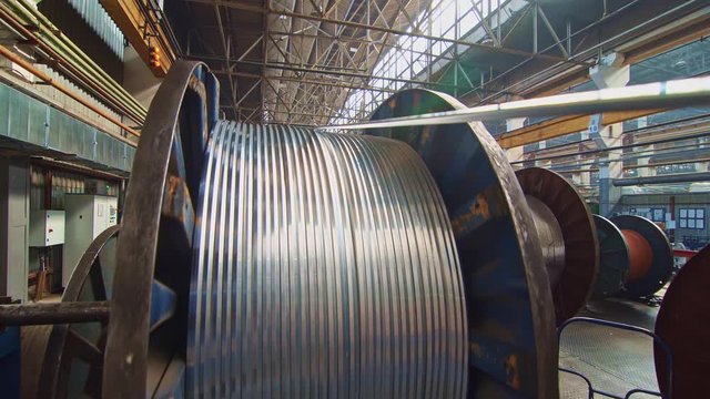 A huge bobbin unwinds a wire in a cable factory. Products are used in energy, transport, construction, engineering, nuclear, defense, oil and gas industries.
