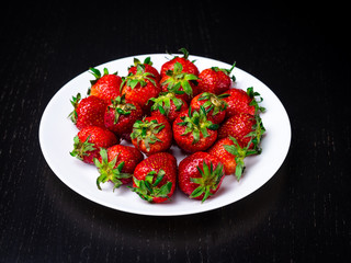 Fresh red strawberry on white ceramic plate on dark background