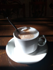 cup of cappuccino with a teaspoon on a saucer in the morning on the table with beautiful shadows from the window