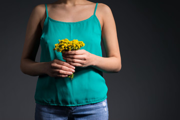 closeup, girl holds yellow flowers, wearing a turquoise T-shirt. Studio photo on a gray background. Spring concept with yellow flowers. Give spring warmth