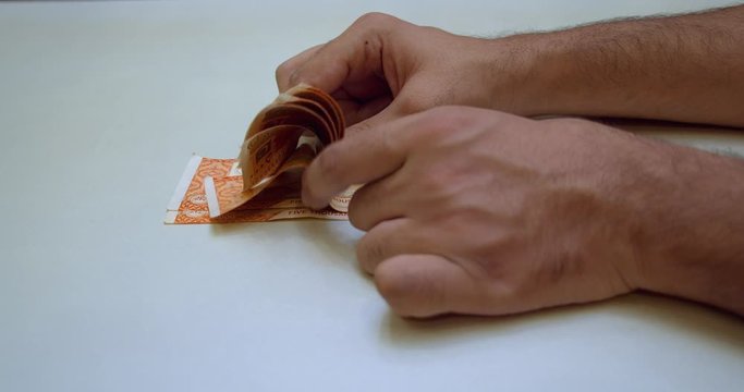 Close up of male hands counting 5000 bills of Pakistani currency on white table