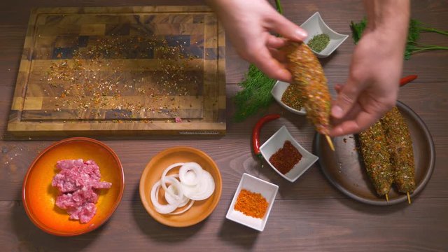 Lulia kebab, a dish of Georgian cuisine. Process of making kebab lula, top view. Chef cooks a lula kebab from raw minced meat and sprinkled with spices. Spices and ingredients stand on the table.