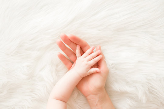 Infant hand on mother palm on white fluffy fur background. Lovely, emotional, sentimental moment. Trust and care concept. Close up. Top down view.